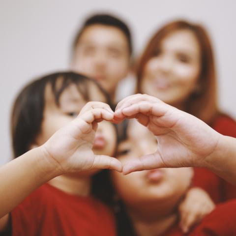 Two children making heart hands, two adults in background