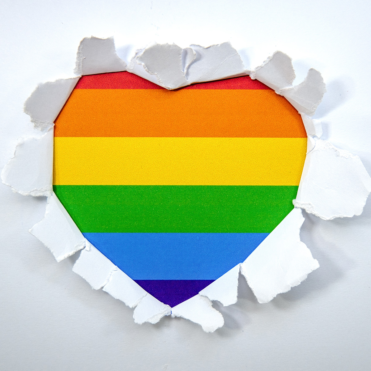 Pride colors are bursting through a blank page forming the shape of a heart