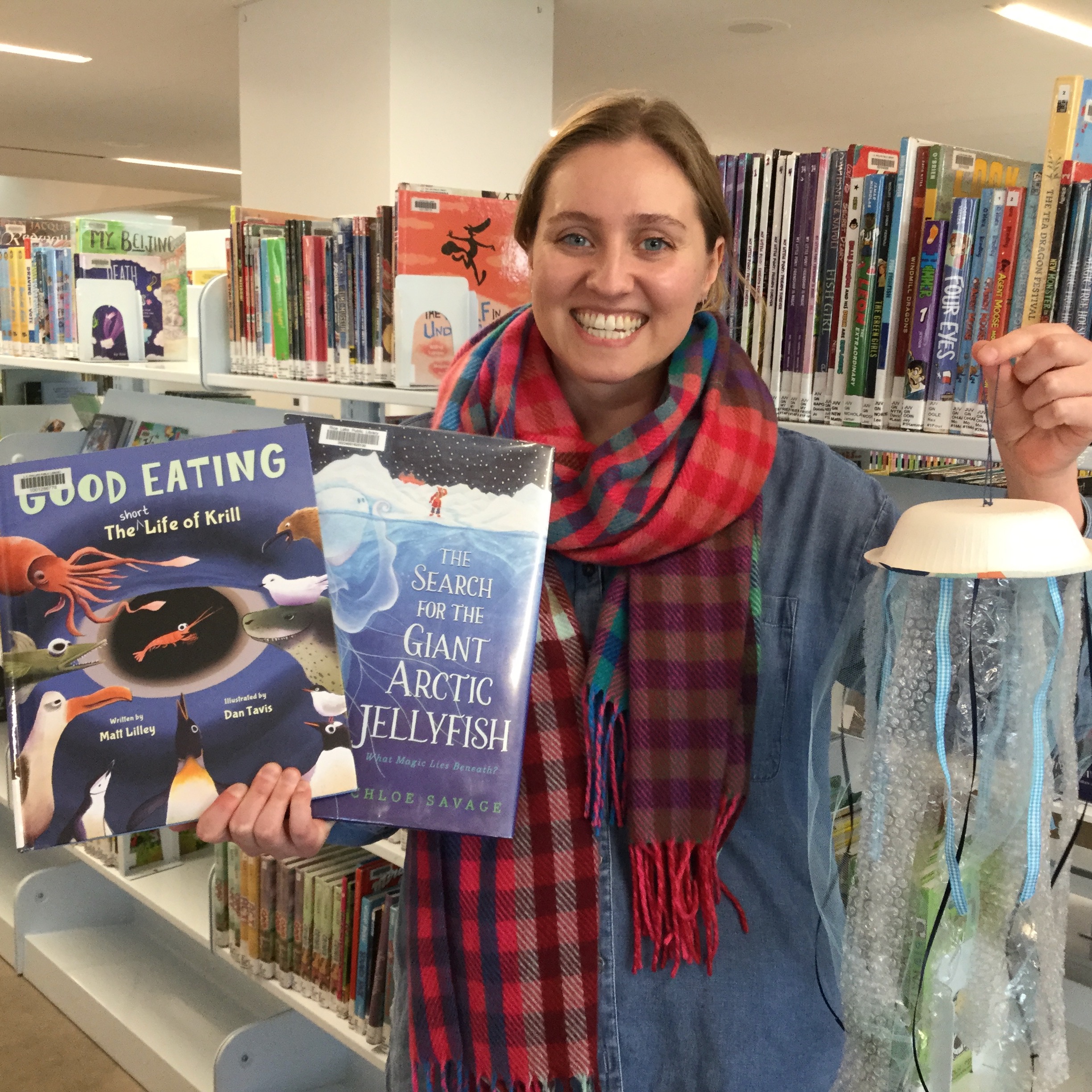 Smiling woman holding two books and a paper jellyfish craft 
