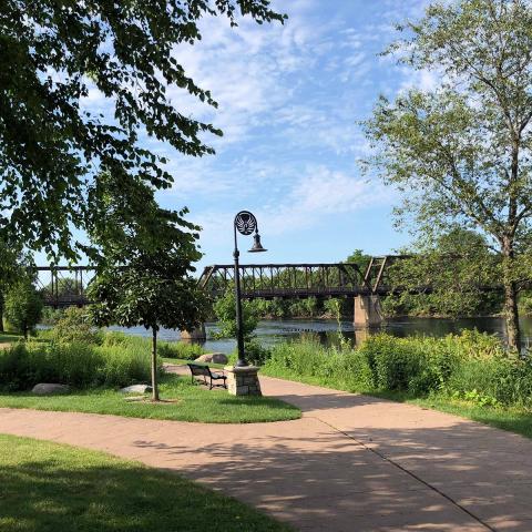 This is a small portion of the walking path in Phoenix Park. Phoenix Park is at the confluence of the Eau Claire and Chippewa Rivers in downtown Eau Claire. One of Eau Claire's many pedestrian bridges over the river is seen in the background. A phoenix is depicted in the metalwork at the arch of lamp post.