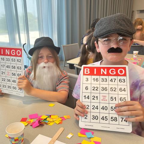 Two boys wearing fake facial hair, holding up BINGO cards