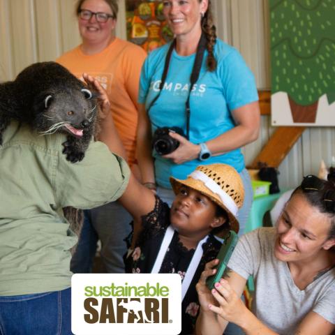 A group of people looking at an animal on a handler's shoulder. 