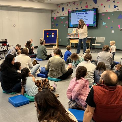 A group of families sitting and watching a woman read a story. 