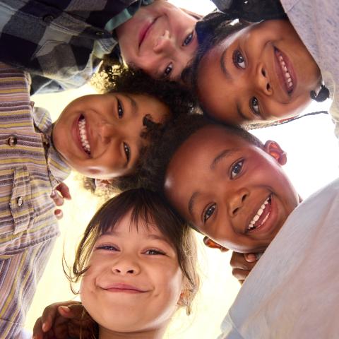 A circle of diverse children looking down at the camera, smiling.