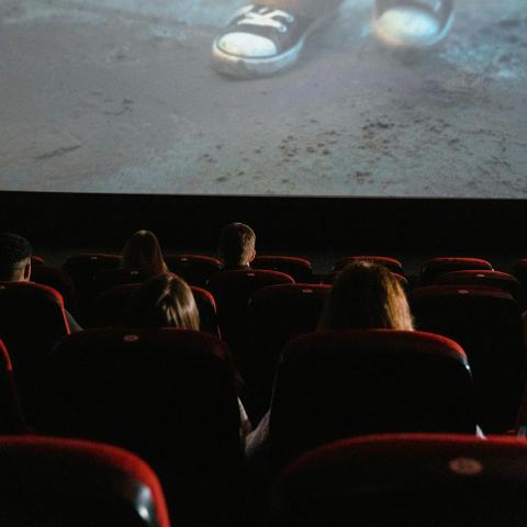 View from the back of a movie theater, looking at rows of filled seats and a screen.