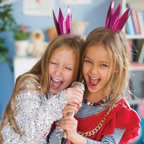 Two young girls wearing matching princess outfits singing into a microphone.