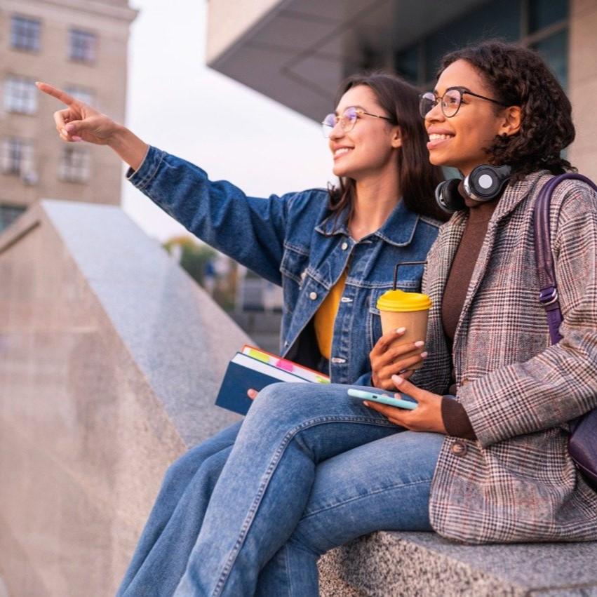 Two students sitting on a step, looking happy