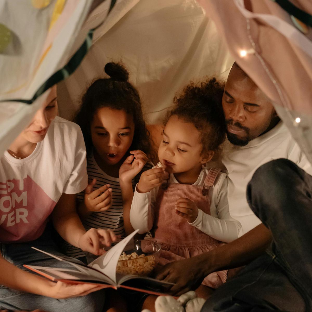 Family of four in a blanket fort, reading a story