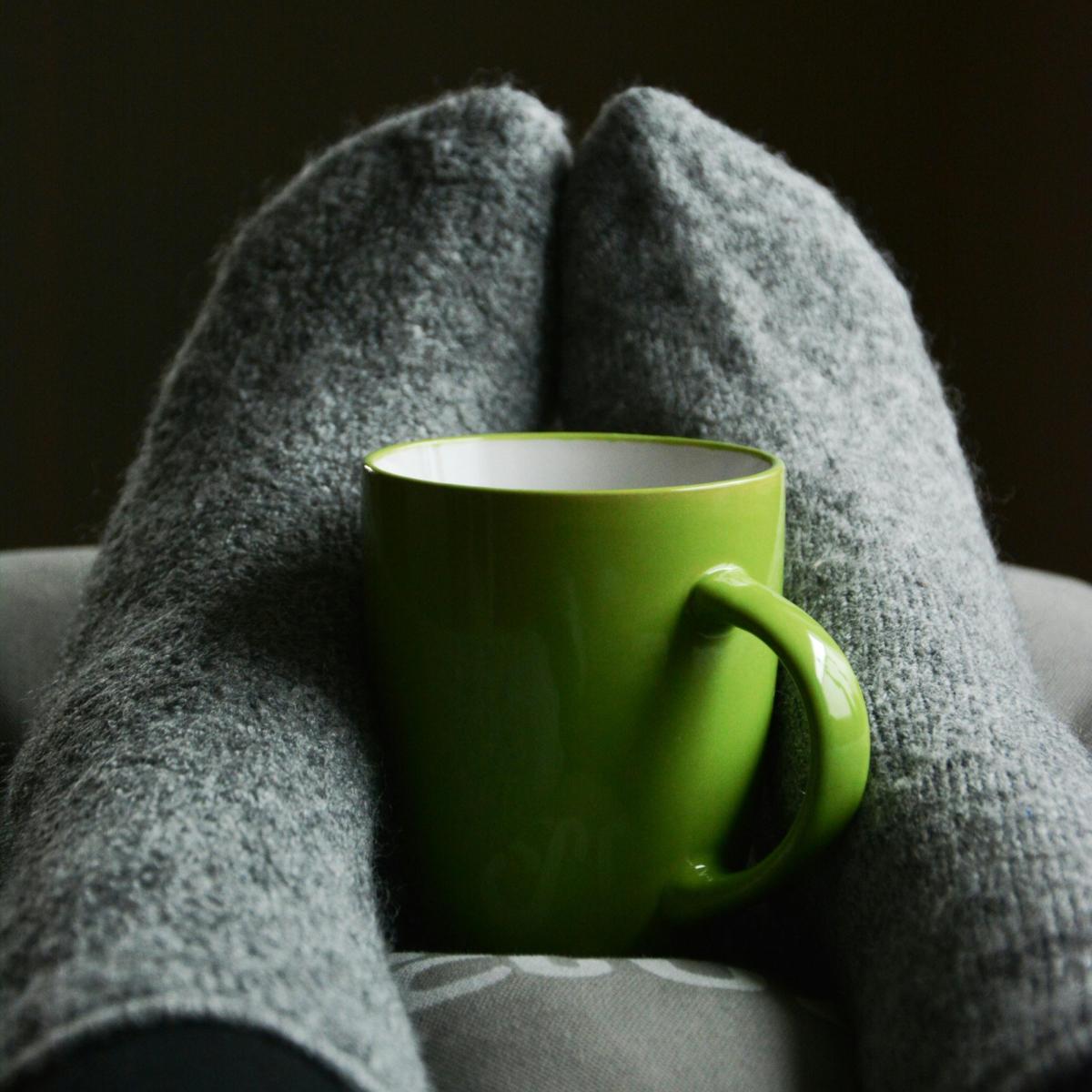 Pair of feet in cozy grey socks, cradling a green mug.