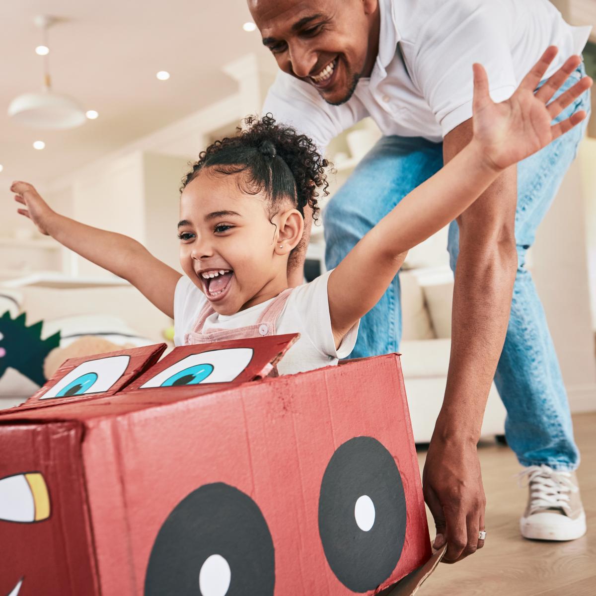 Grown-up pushing decorated cardboard box with child passenger. 