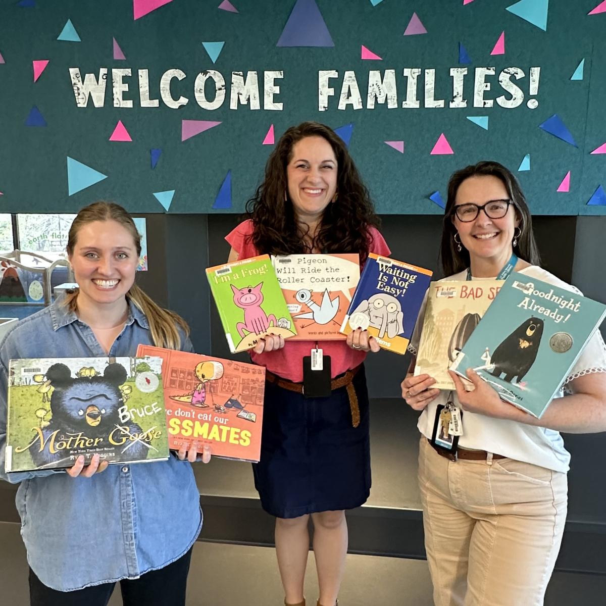 Three women standing in a row, holding books and smiling.